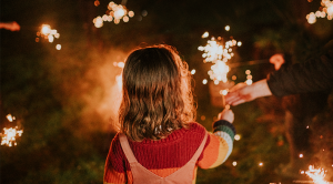 A child holds a sparkler in the darkness, surrounded by other burning sparklers